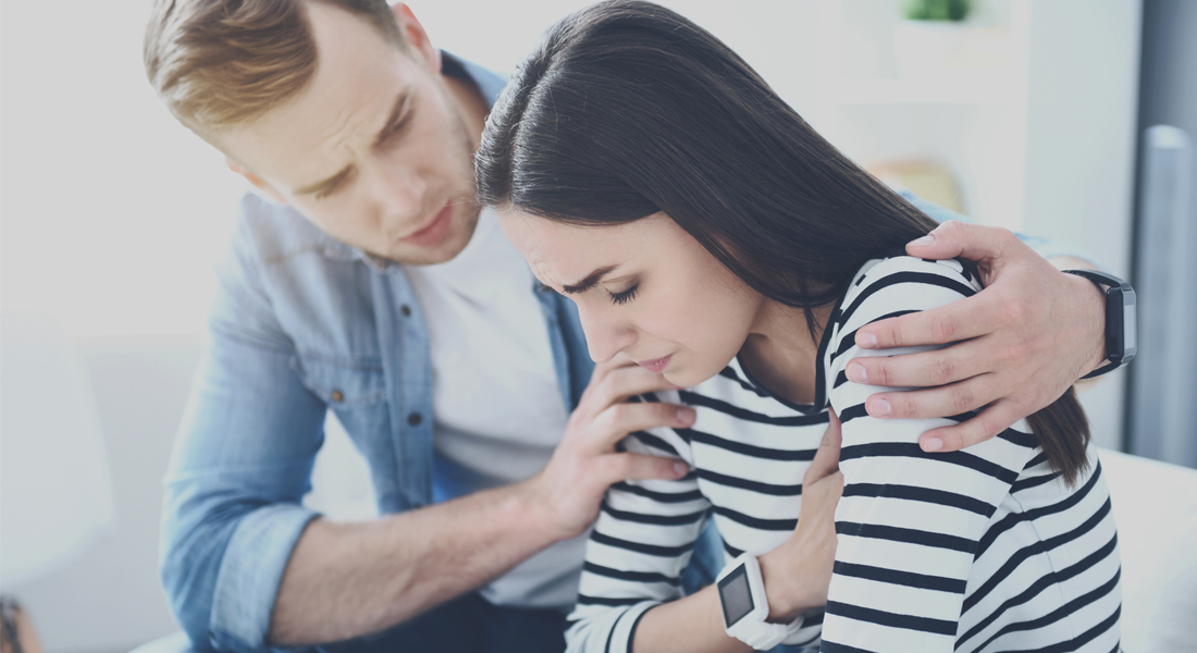 Photo of a woman sitting in a couch looking at a smartwatch and feeling anxious