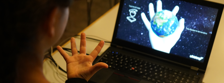 Person with their hand open in front of a computer with a hand holding the Earth on the display