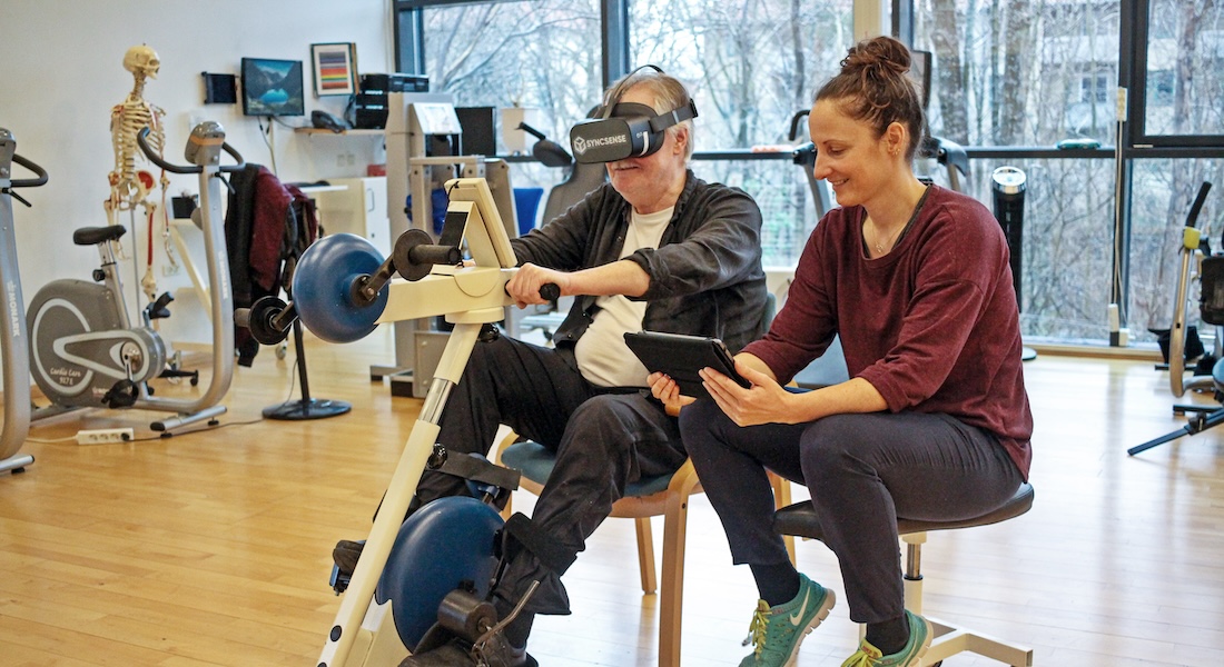 Man in fitness centre wearing VR glasses, guided by female physiotherapist